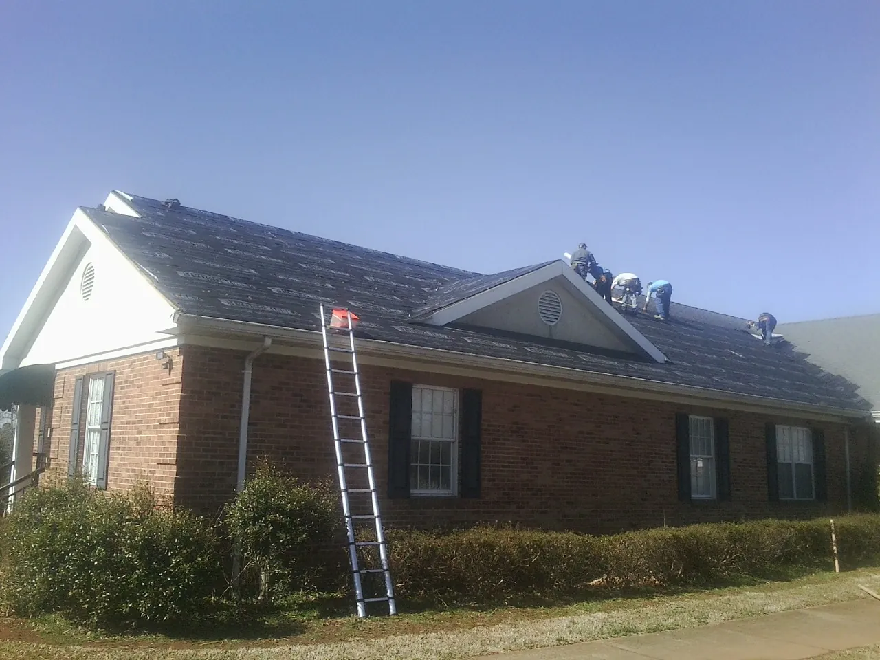 Crew tearing shingles off a brick ranch roof with a ladder set — Metal Roof Repair work by our crew in Port Costa