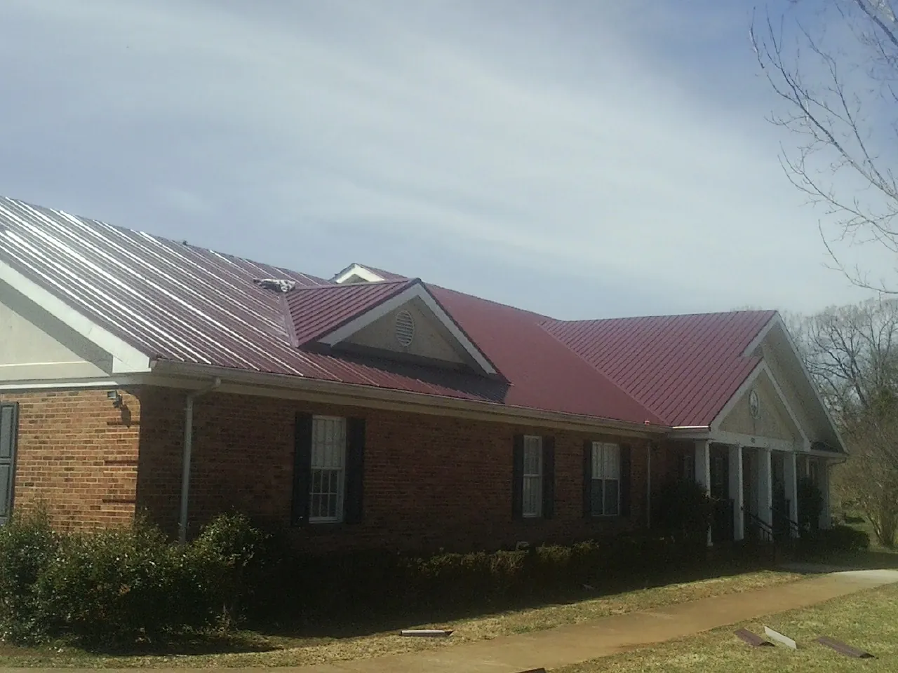 Red metal roof with gabled entries on a long brick building, from a Hail Damage Roof Repair job in Port Costa