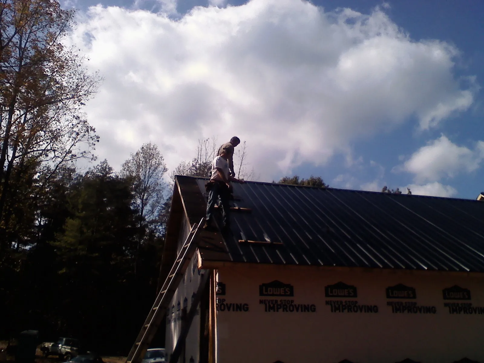 Roofer fastening dark metal panels high against a cloudy sky, from a Roof Inspection job in Port Costa